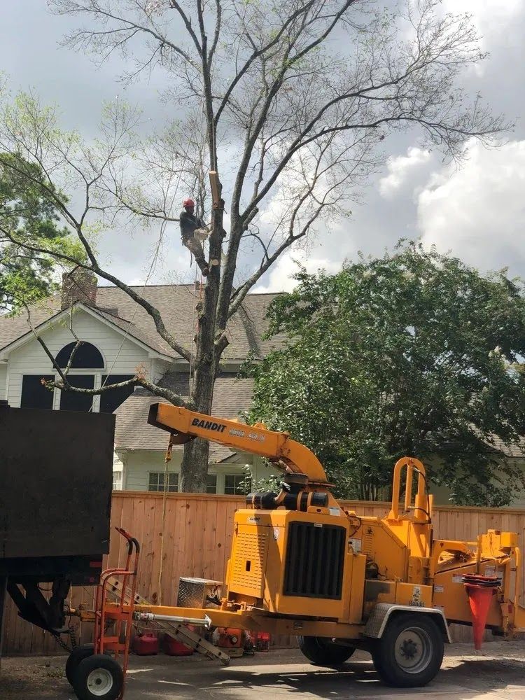 Yellow utility truck with boom lift working beside a house and large tree in a yard