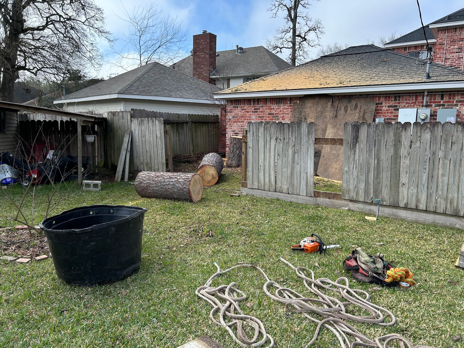 Backyard with a large black tub, coiled ropes on grass, and a wood fence beside a brick house