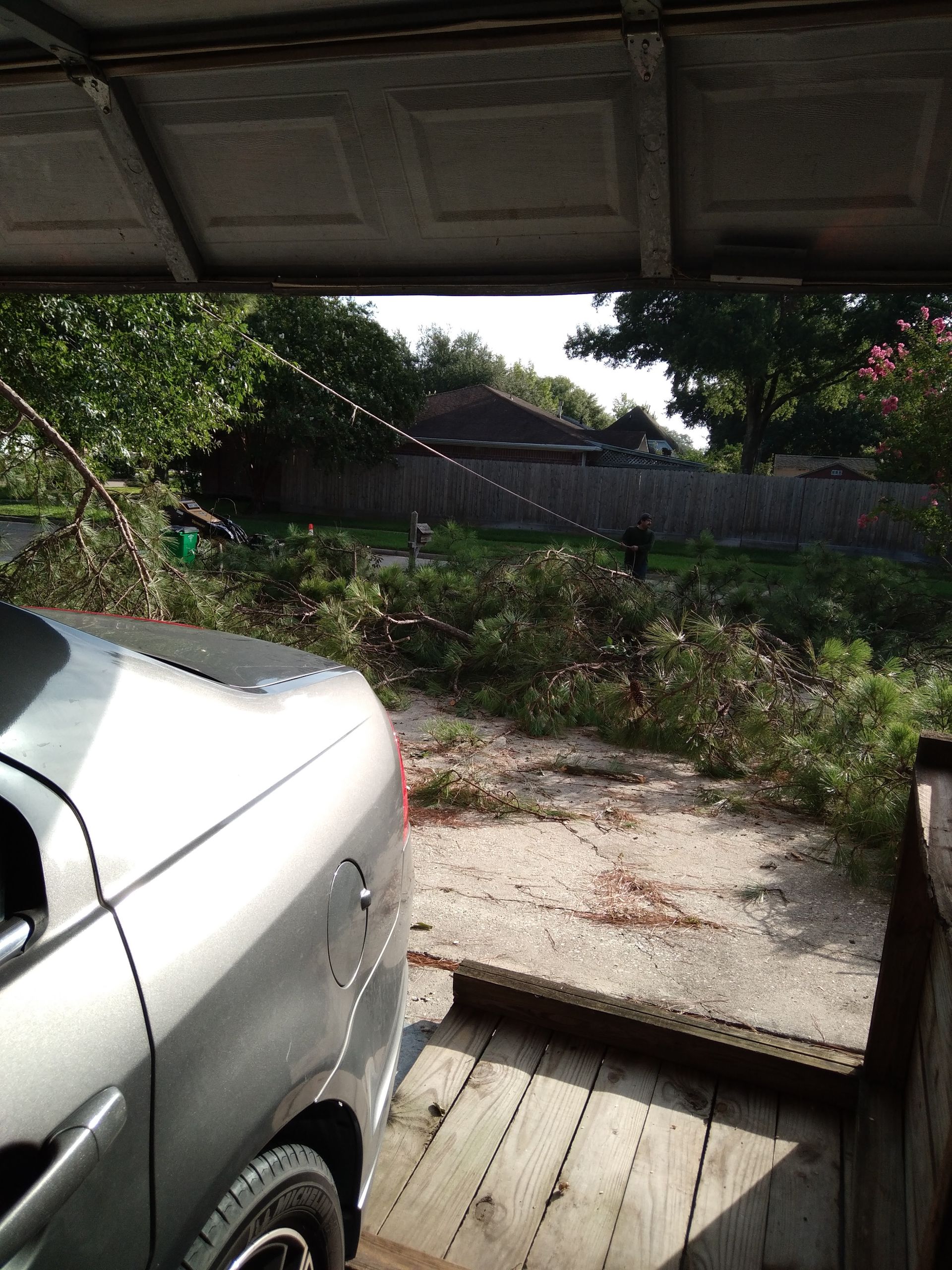 Car parked under a roof, looking out onto a grassy backyard with a fence and trees.