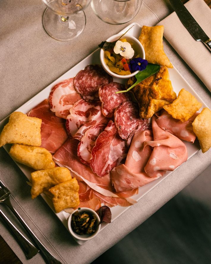 Tagliere di salumi su un piatto bianco con carne, pane fritto e salse.