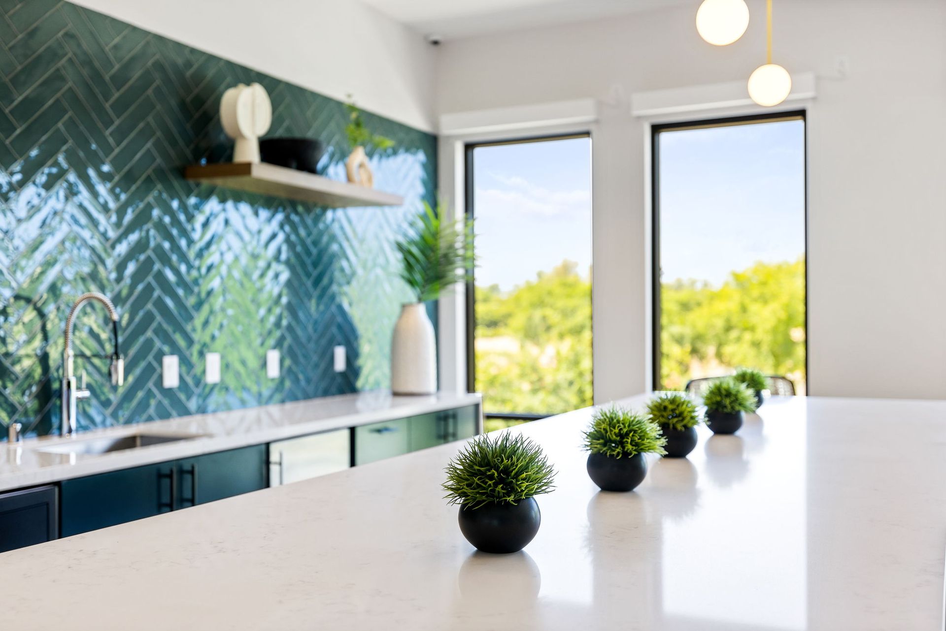 Bright modern kitchen with teal backsplash, white island, and small potted plants by a sunny window at The Hayley.