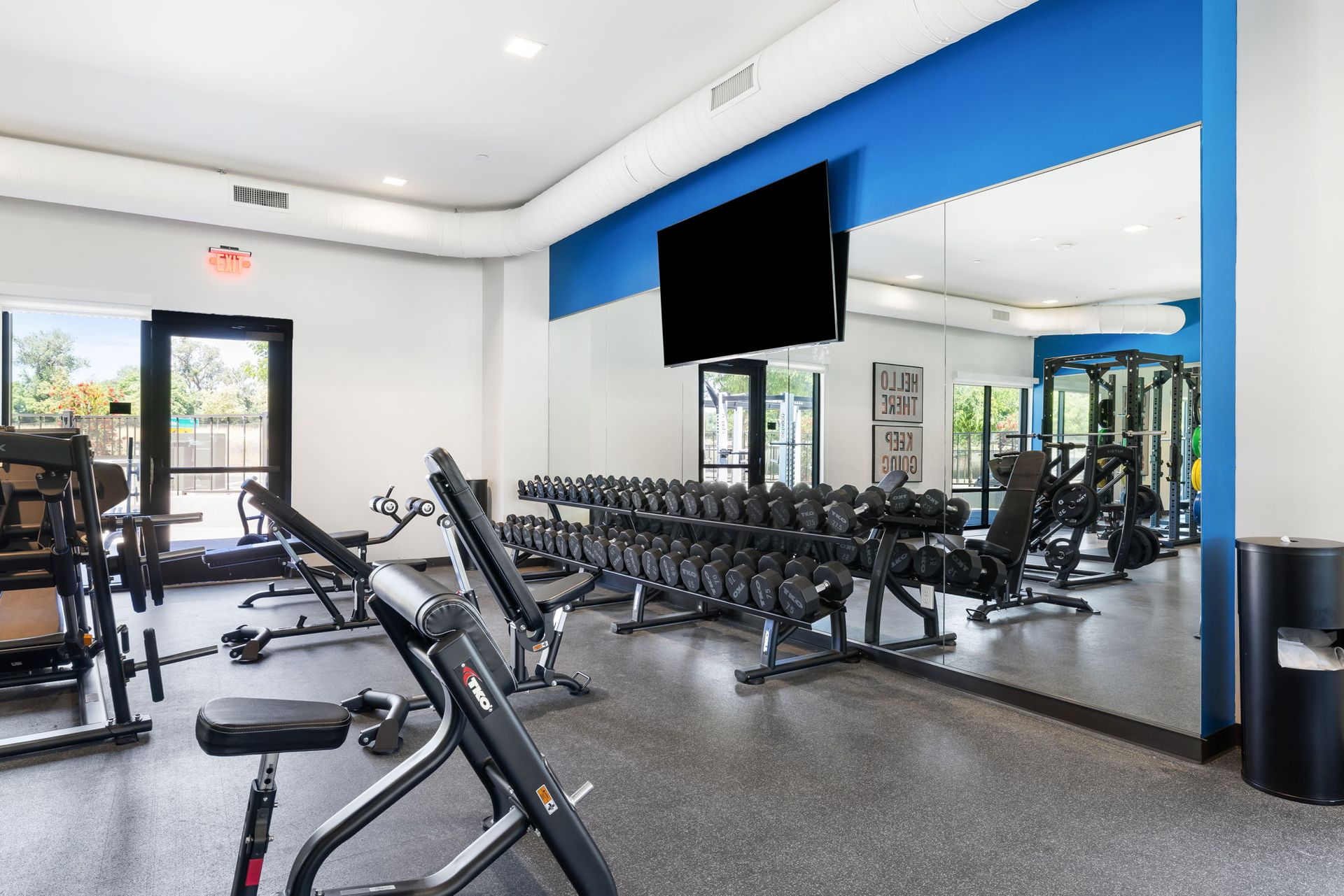 A gym with a lot of dumbbells and a flat screen tv on the wall.