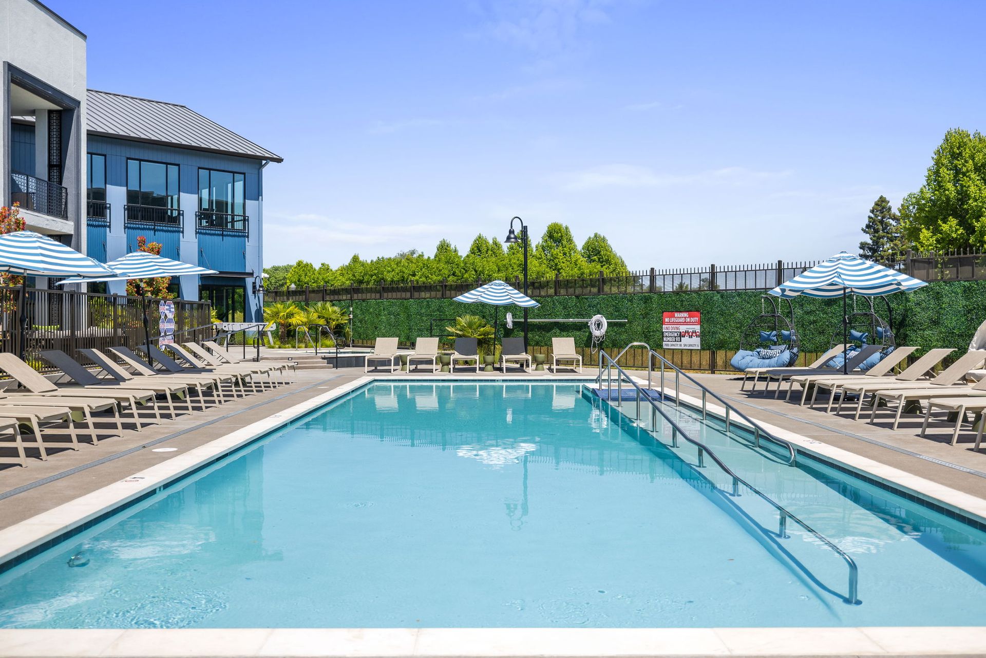 A large swimming pool surrounded by chairs and umbrellas in front of a building at The Hayley, offers apartments in Sacramento, CA.