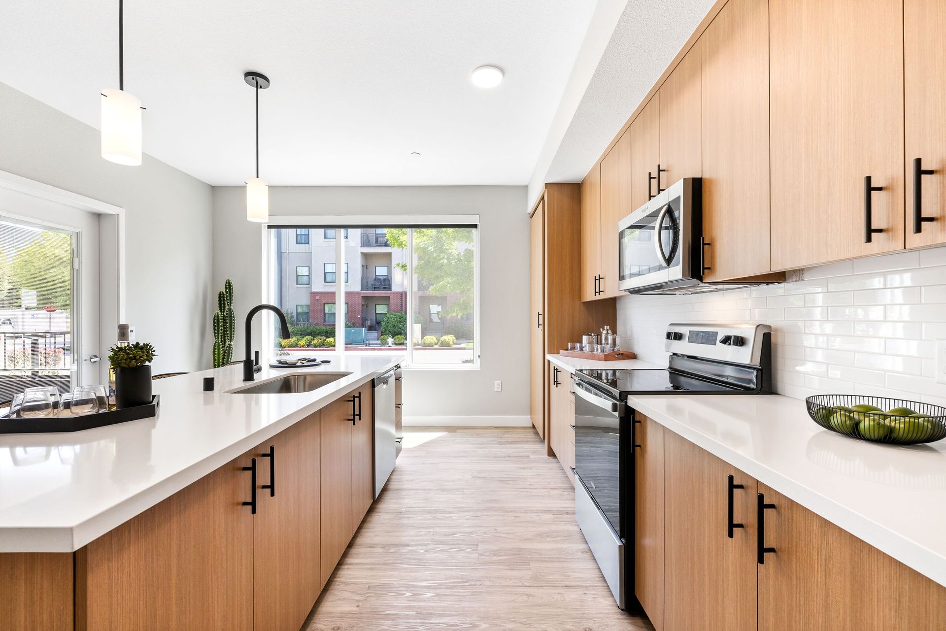 A kitchen with wooden cabinets , white counter tops , stainless steel appliances and a large window.