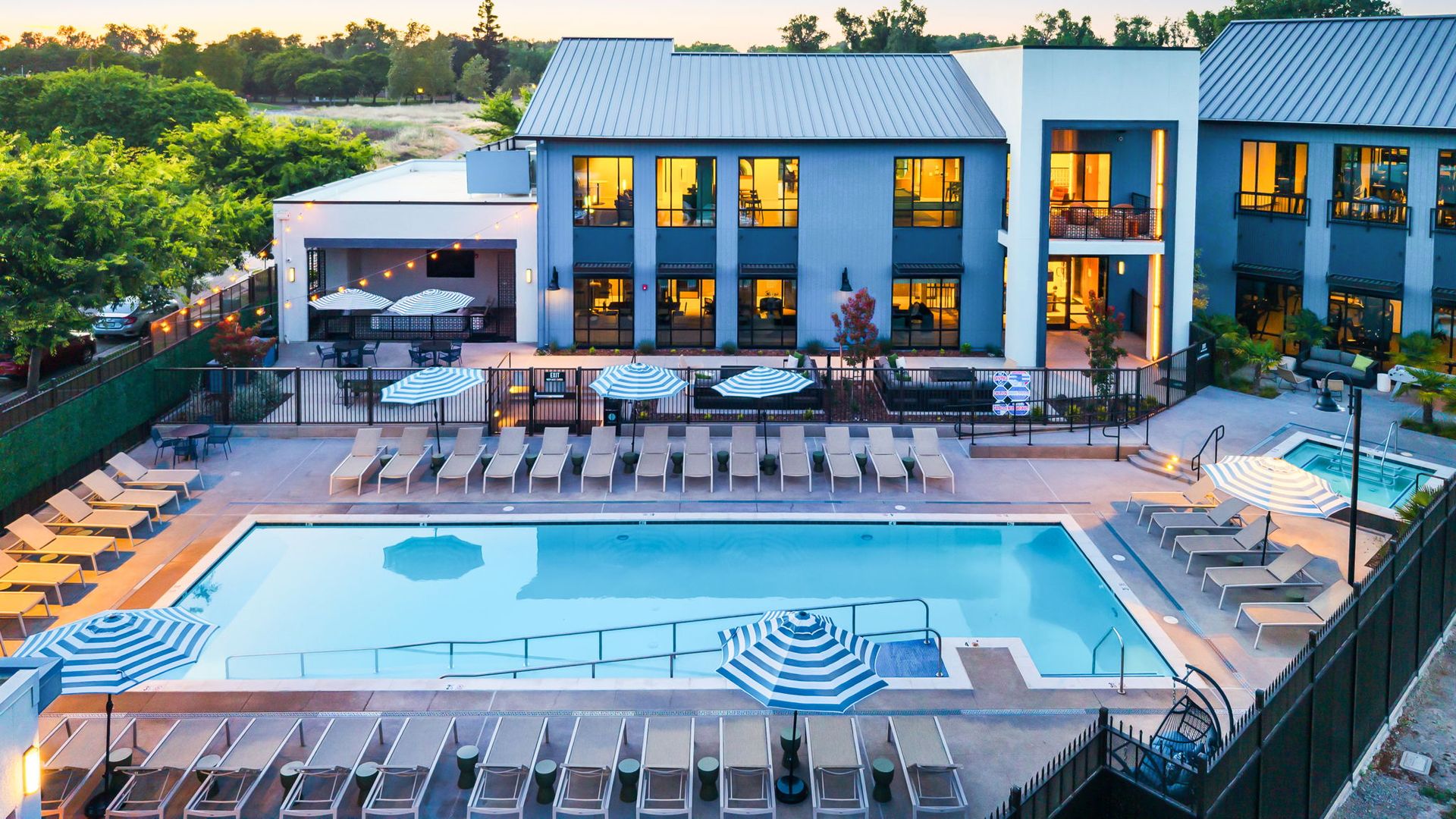 An aerial view of a large swimming pool surrounded by chairs and umbrellas in front of a large building.