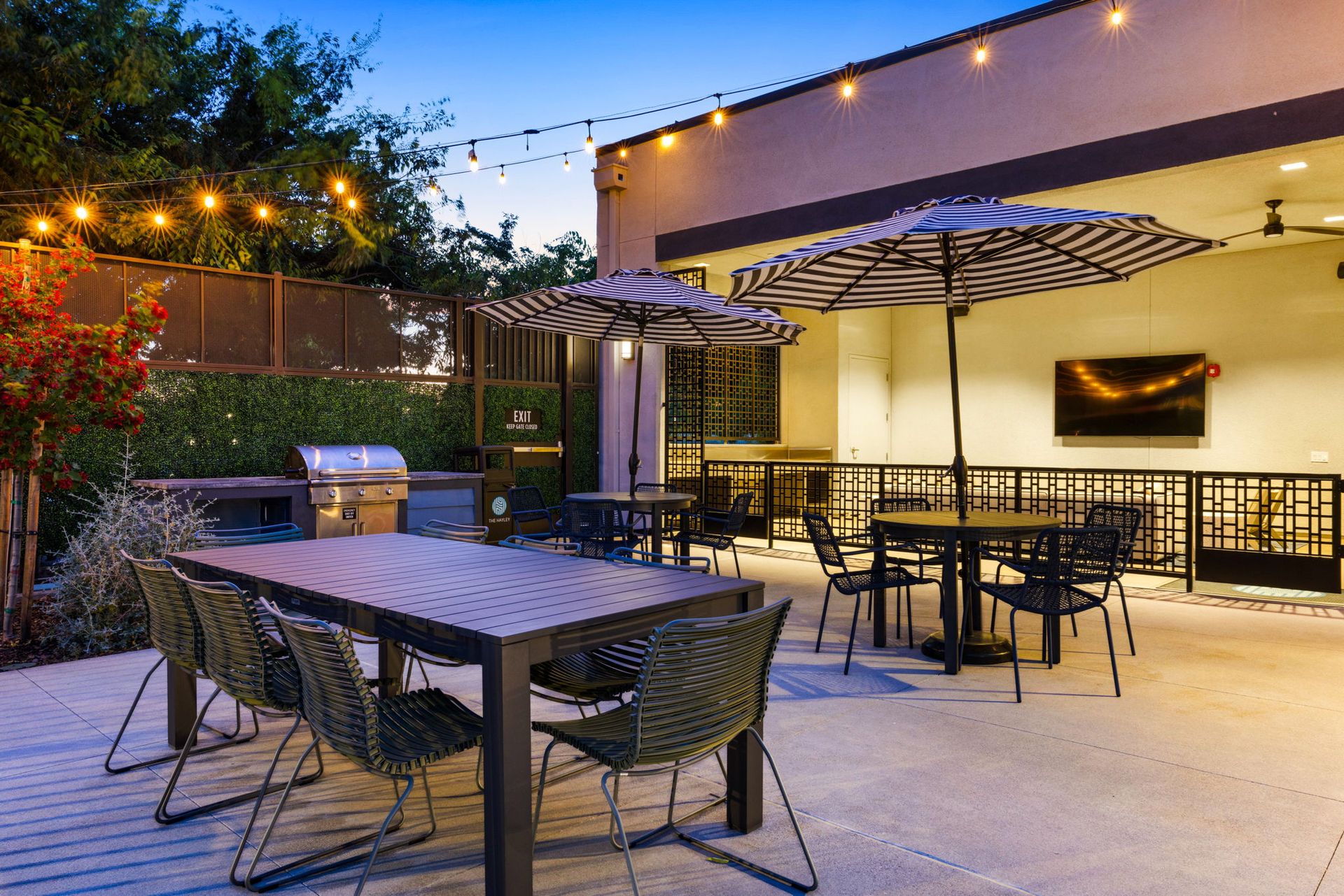 A patio with tables , chairs , umbrellas and a grill.