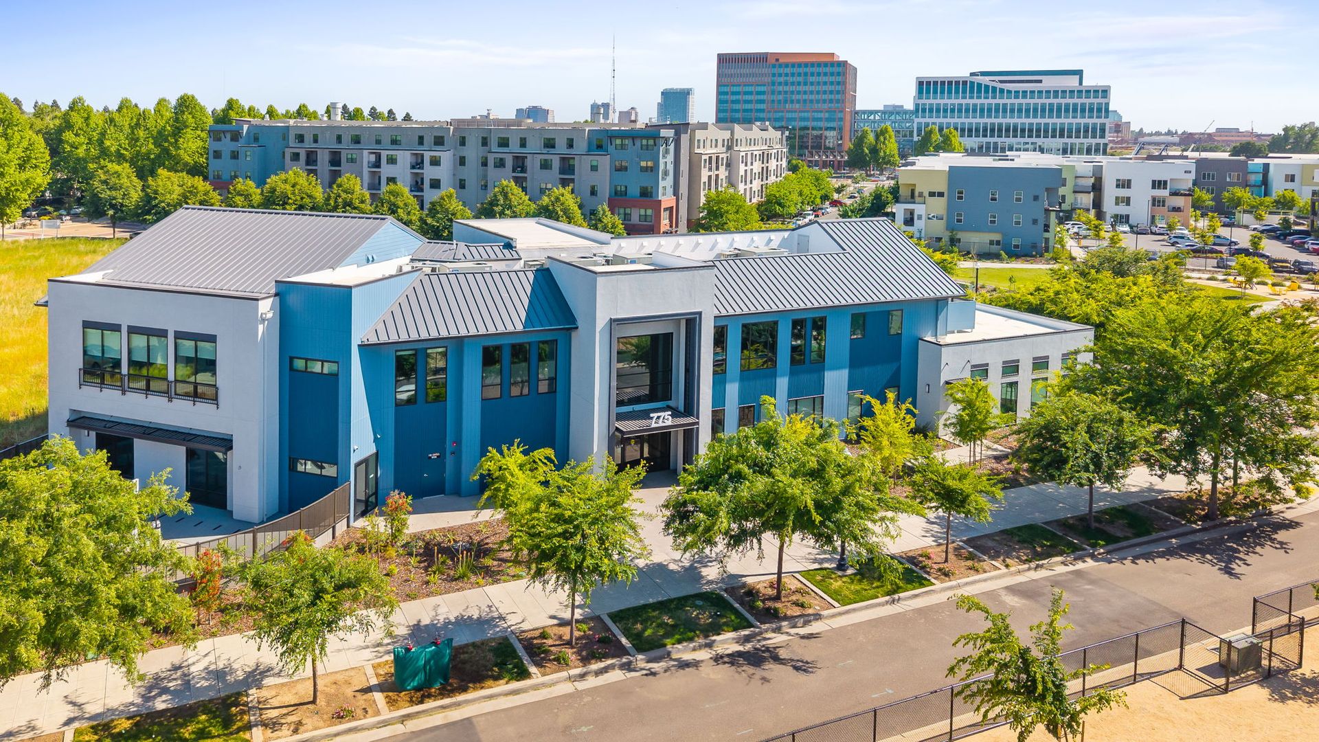 An aerial view of a large blue and white building surrounded by trees at The Hayley, offers apartments in Sacramento, CA.