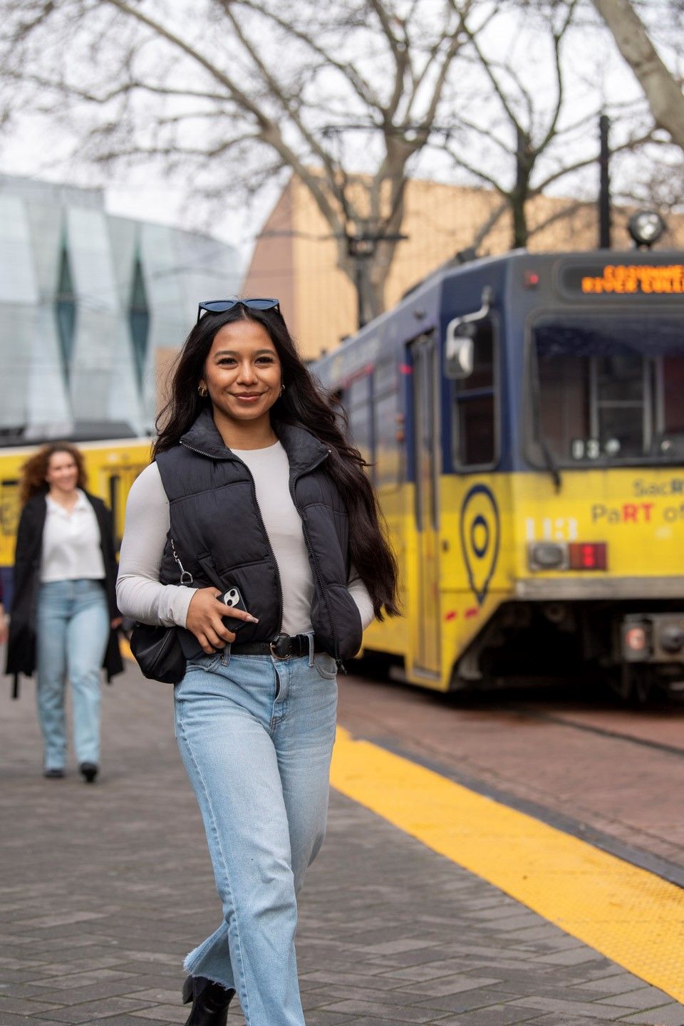 A woman is standing in front of a yellow train.