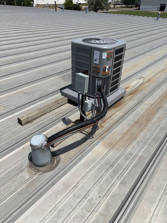 Gray rooftop HVAC unit with connected pipes mounted on a metal roof. Gray rooftop HVAC unit with connected pipes mounted on a metal roof.