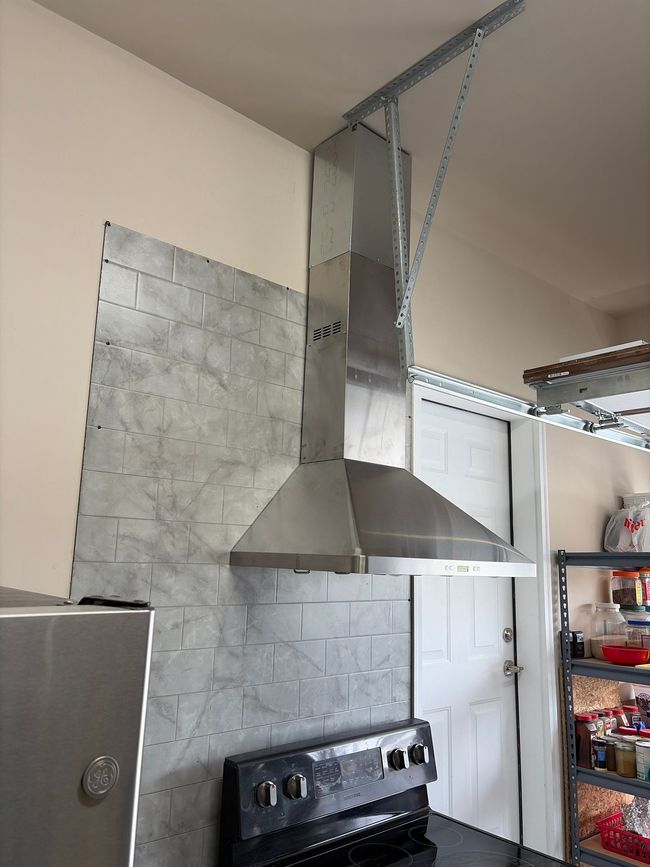 Kitchen with stainless steel range hood, stove, white door, and shelves against a gray tiled wall. Kitchen with stainless steel range hood, stove, white door, and shelves against a gray tiled wall.