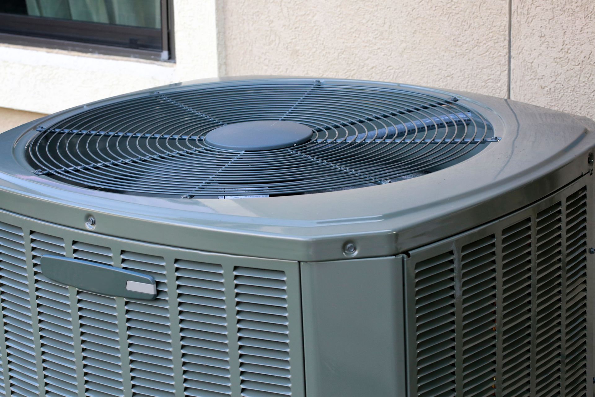 Outdoor air conditioning unit with large black fan on top beside a building wall Outdoor air conditioning unit with large black fan on top beside a building wall