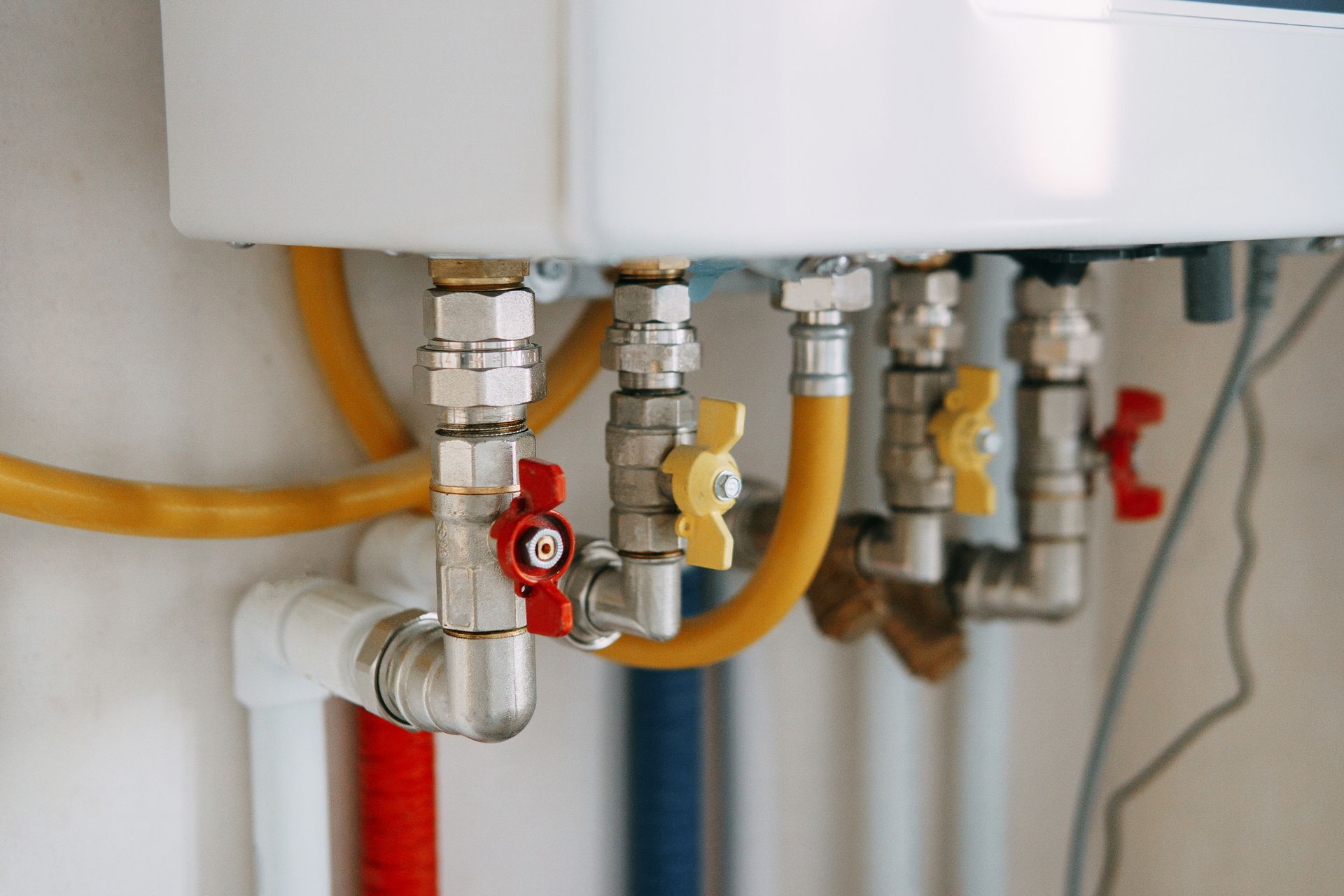 Close-up of water heater pipes and valves with red and yellow shutoff handles under a sink or tank. Close-up of water heater pipes and valves with red and yellow shutoff handles under a sink or tank.
