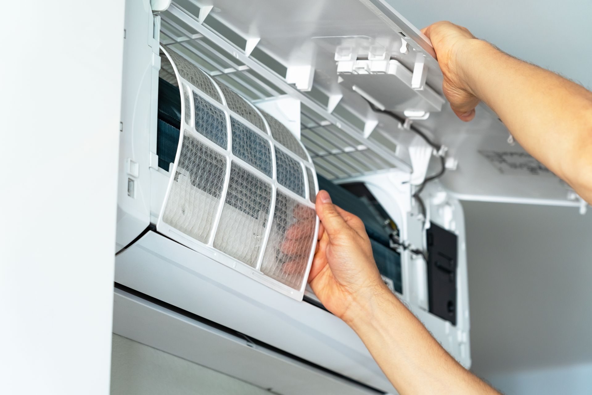 Hands cleaning an indoor air conditioner filter with the unit open. Hands cleaning an indoor air conditioner filter with the unit open.