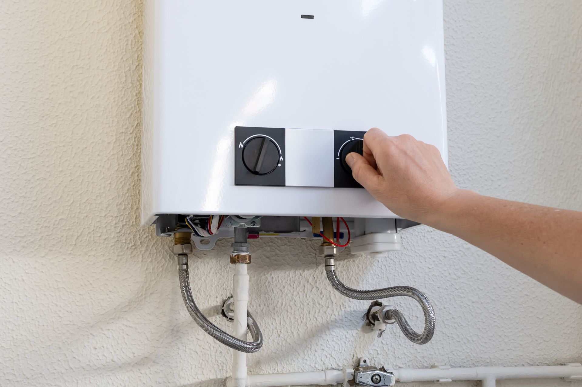 Hand turning the knob on a white wall-mounted water heater with exposed pipes Hand turning the knob on a white wall-mounted water heater with exposed pipes