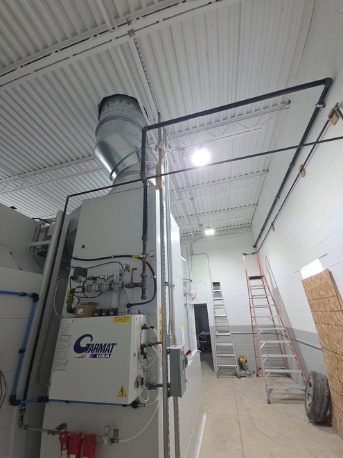 Industrial utility room with large HVAC unit, exposed ductwork, ladder, and concrete floor under bright ceiling lights Industrial utility room with large HVAC unit, exposed ductwork, ladder, and concrete floor under bright ceiling lights
