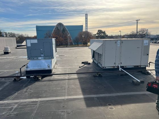 Two white HVAC units on a rooftop at sunset, with buildings and a cloudy sky in the background Two white HVAC units on a rooftop at sunset, with buildings and a cloudy sky in the background