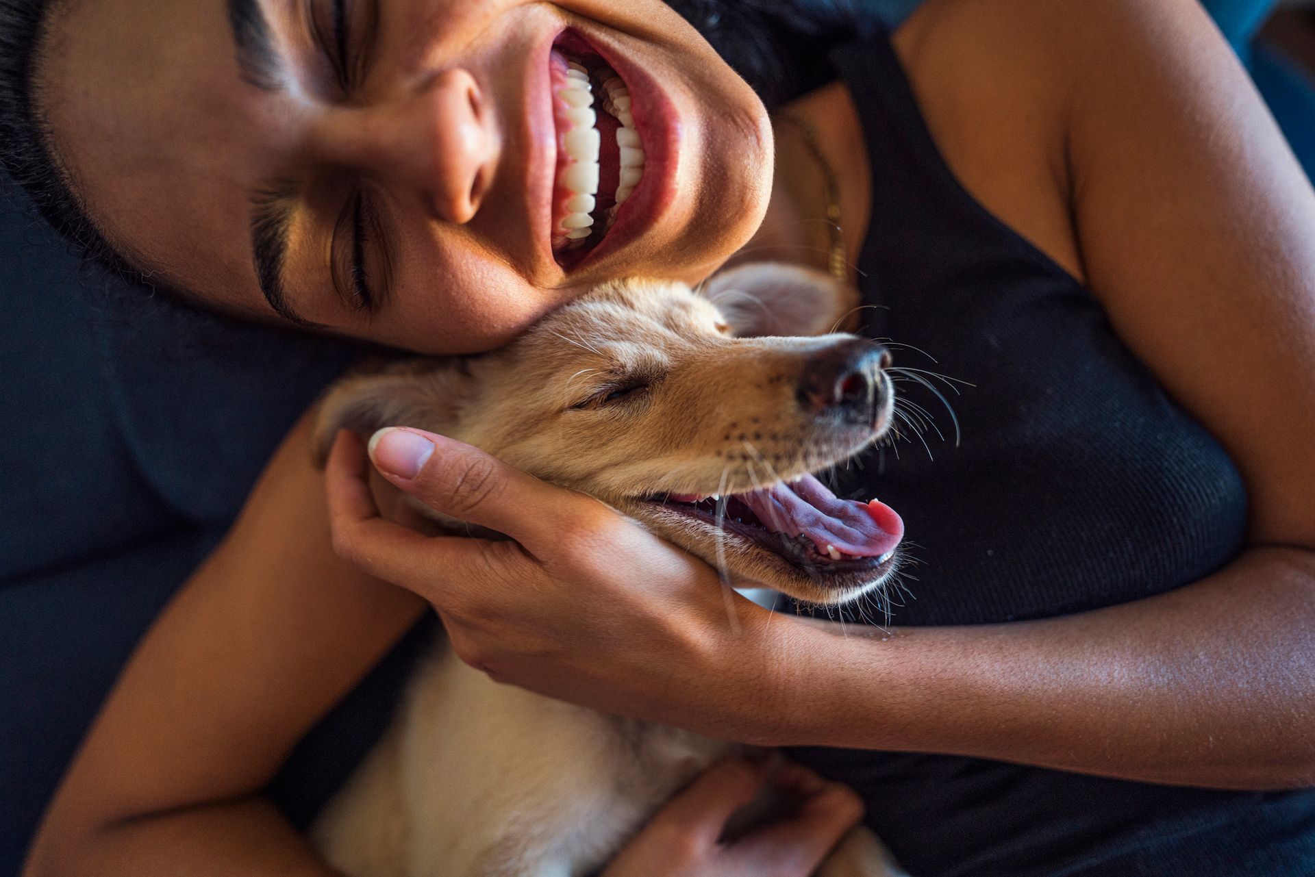 Woman laughing while hugging a small dog, both appearing joyful.
