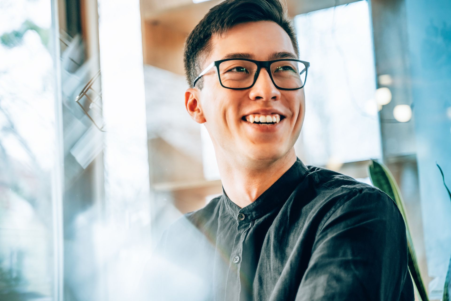 Smiling Asian man wearing glasses, looking off-camera. He's in a bright, modern interior.