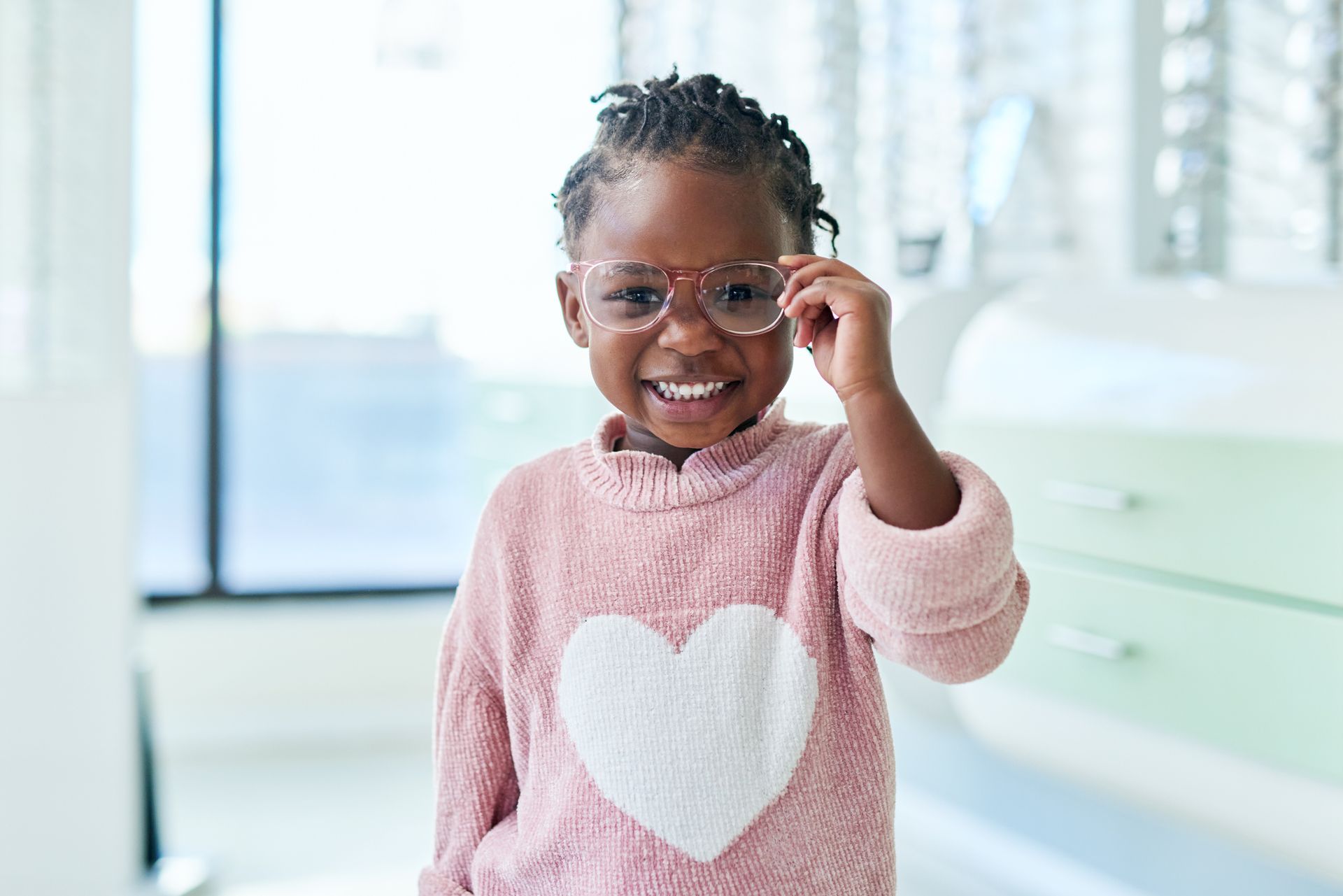 Young Black girl smiles, wearing new glasses in an optician's office.