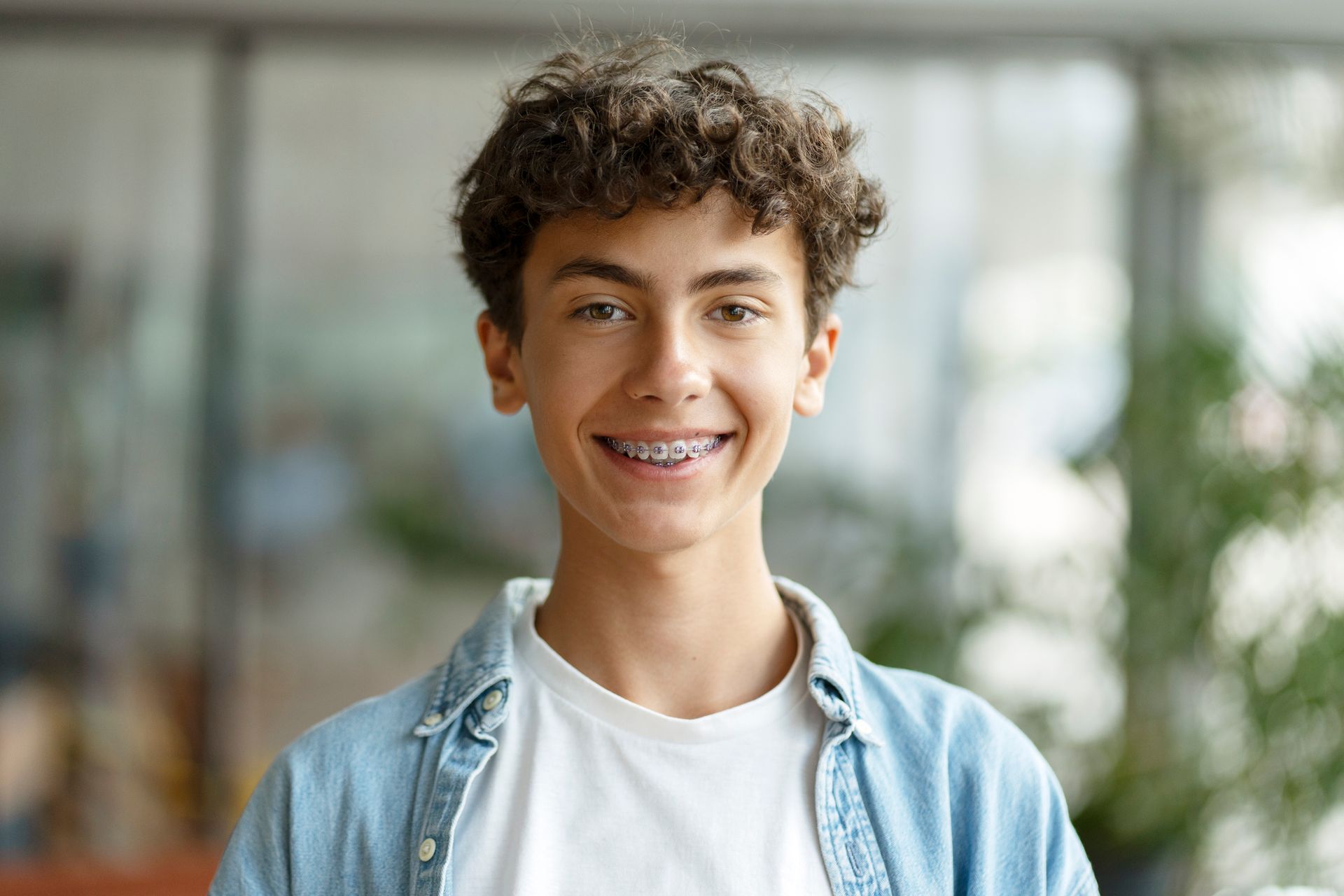 Teenager with curly hair, braces, smiling, wearing a denim shirt and white t-shirt.