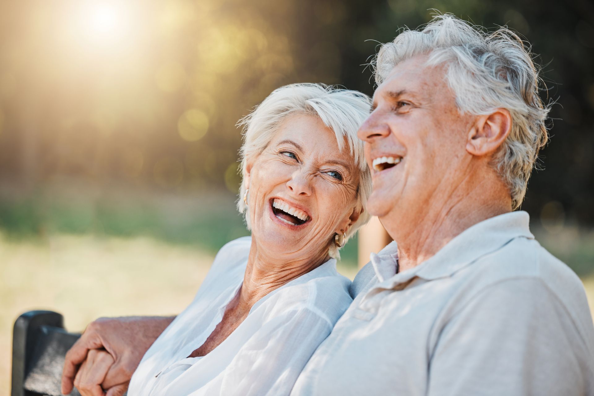 Smiling elderly couple sitting outside, enjoying sunshine, outdoors.
