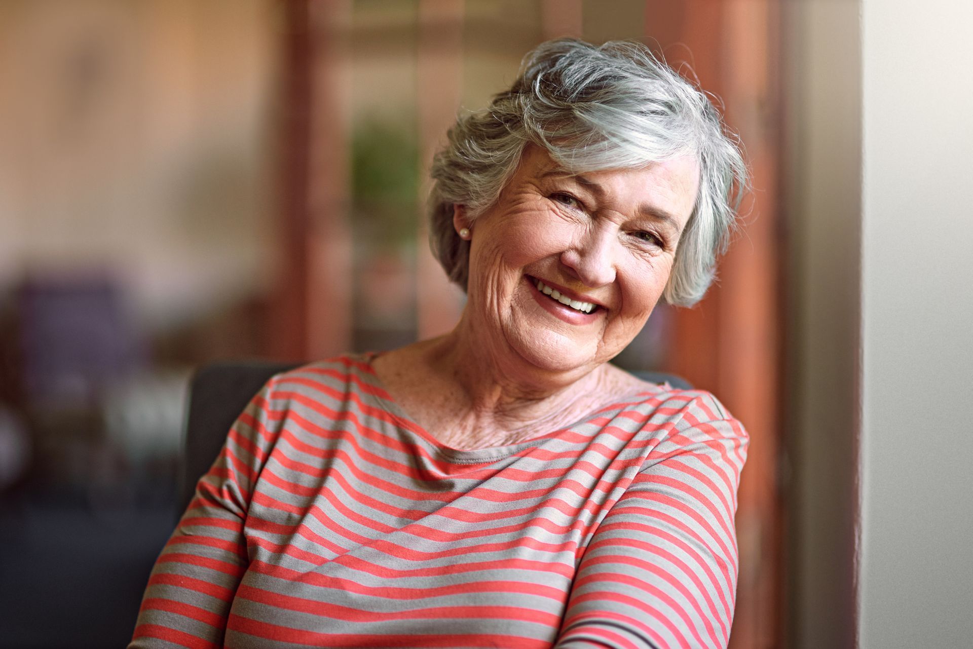 Smiling elderly woman with gray hair wearing a striped shirt, indoors.