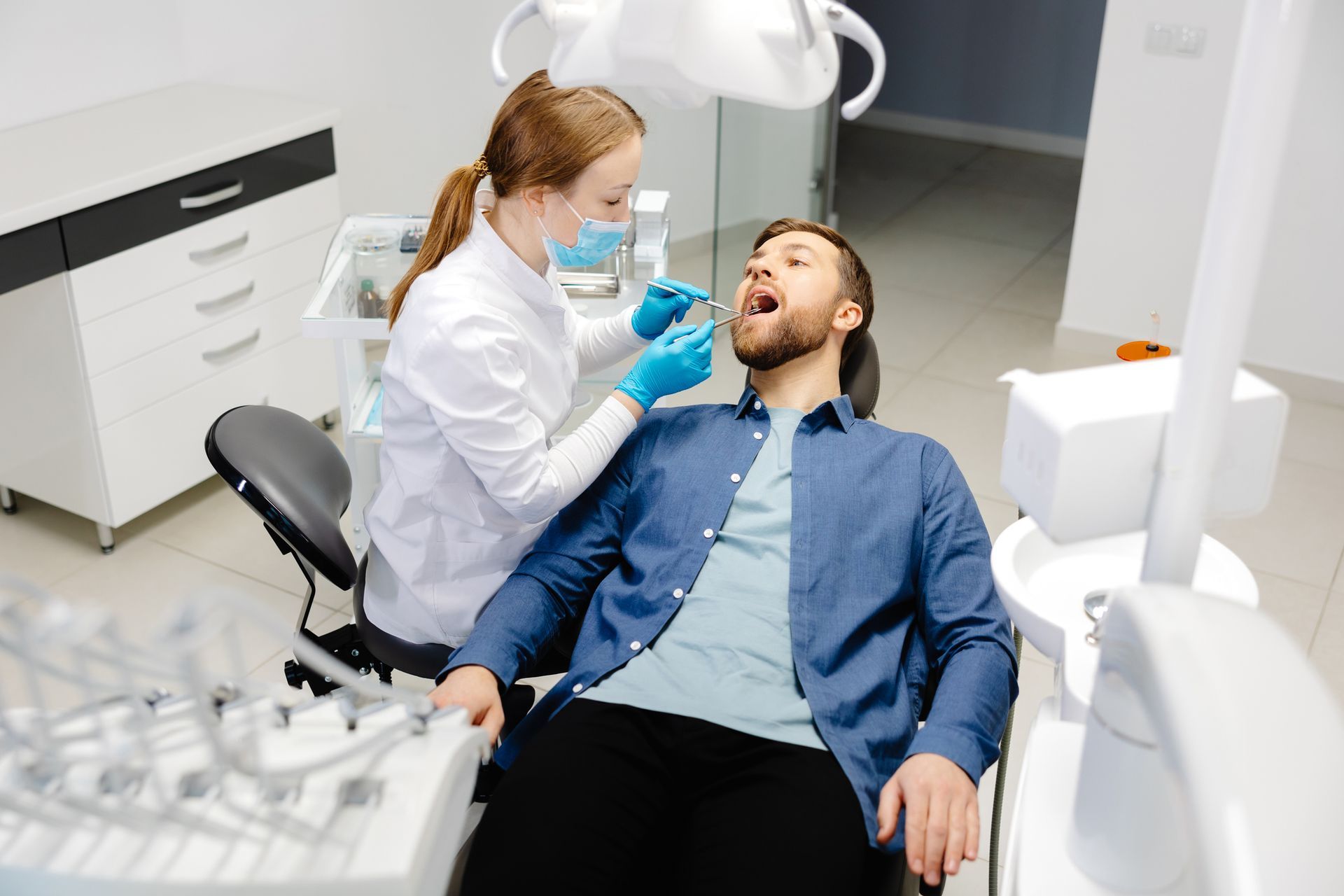 Dentist examining a male patient's teeth in a dental clinic. The patient has mouth open.