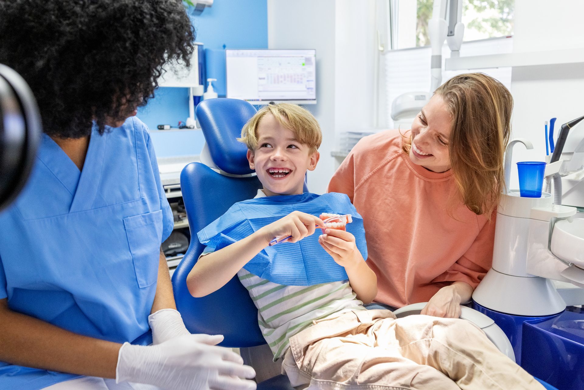 Child at dentist with mother, smiling; dentist in blue scrubs.