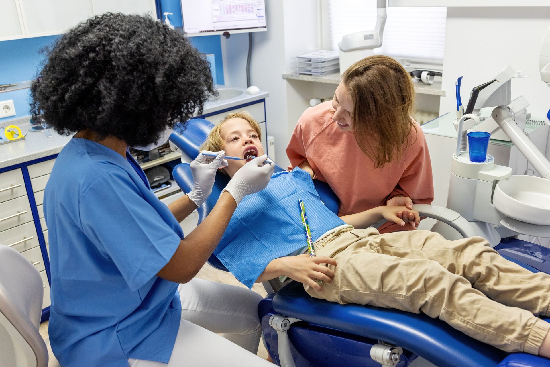 A dentist examines a child's teeth in a dental clinic, with the mother present.