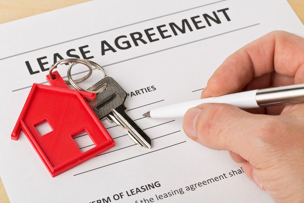 Man holding pen over house door key with red keychain pendant and lease agreement - Lawyer in Woy Woy, NSW