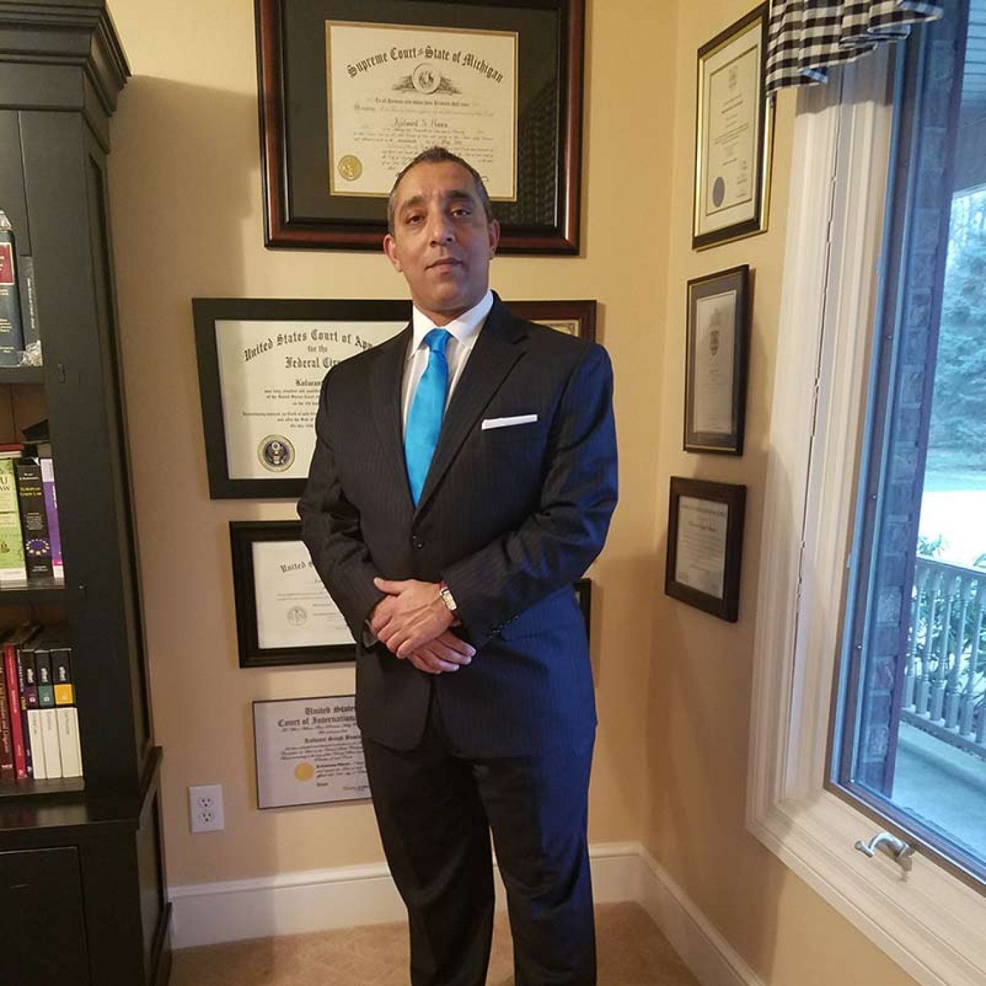 A man in a suit and tie is standing in a room with framed diplomas on the wall