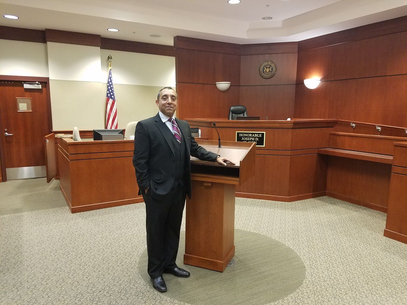 A man in a suit and tie is standing in front of a podium in a courtroom.