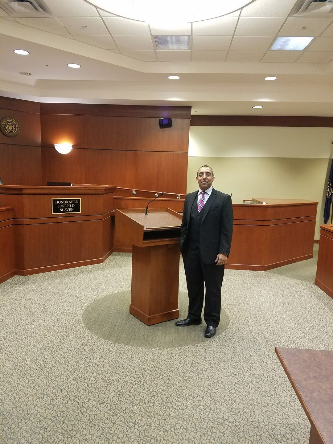 A man in a suit and tie is standing in front of a podium in a courtroom.