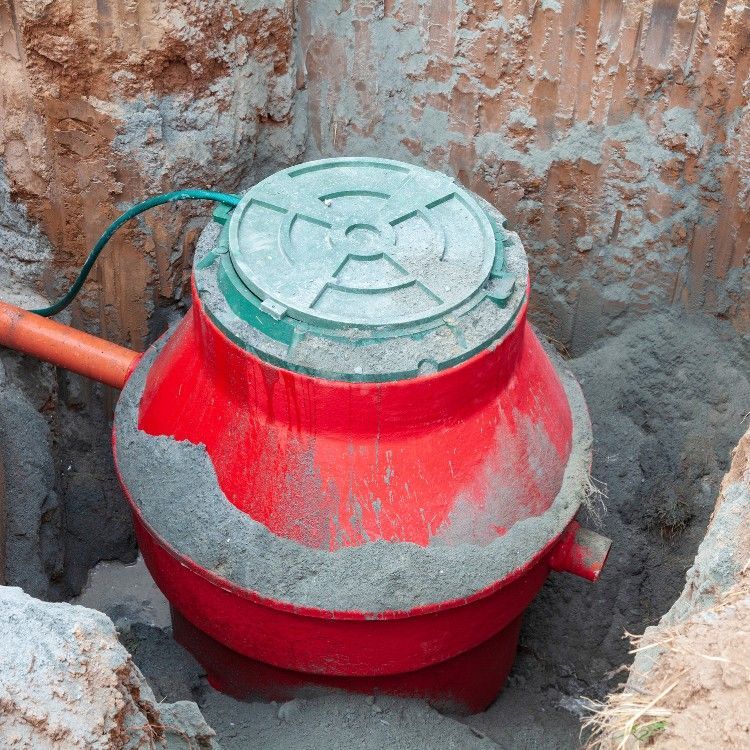 Red cylindrical underground tank with a green lid and gray coating in an excavated pit.