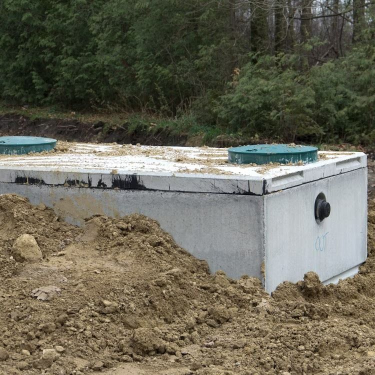 Concrete utility tank in a muddy clearing, with green covers on top and a wooded background