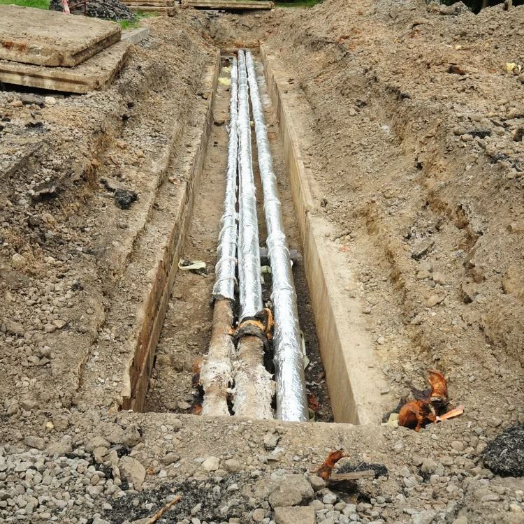 Trench with exposed white utility pipes laid in the dirt at a construction site