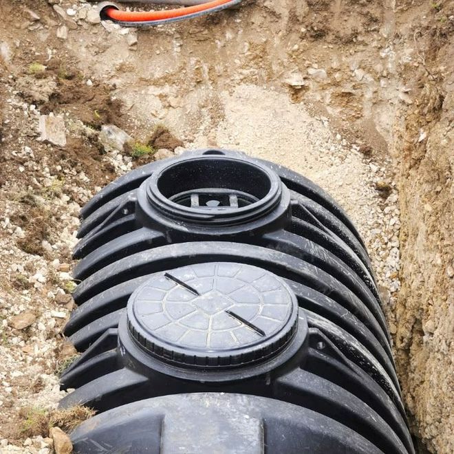 Black ribbed septic tank buried in a dirt trench with two circular access lids visible