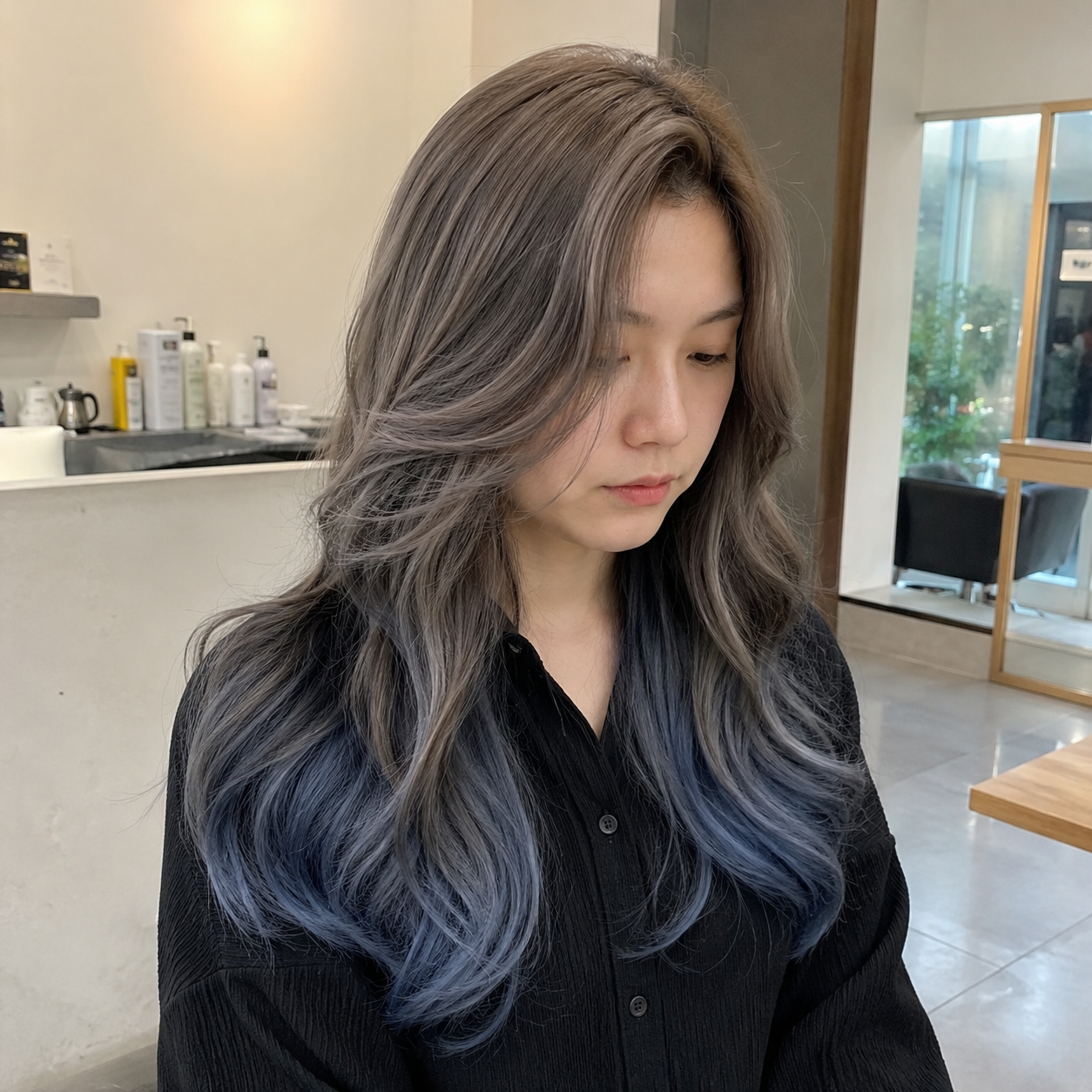 Woman with long wavy gray-blue hair looking down in a bright salon interior at busan gwangalli haeundae