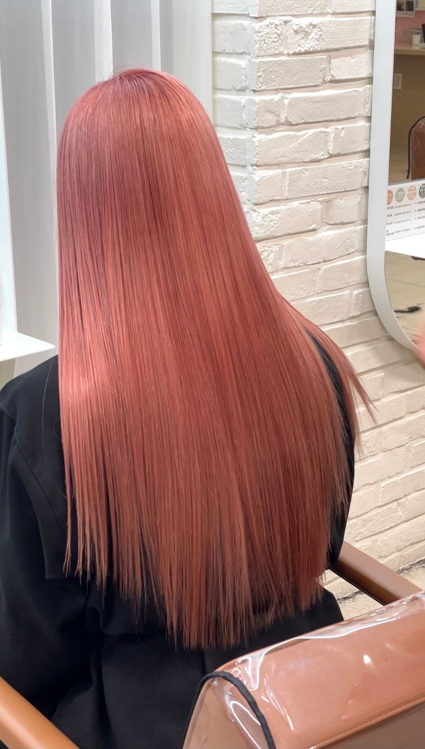 Long straight pink hair from the back in a salon chair beside a white brick wall. at busan gwangalli haeundae