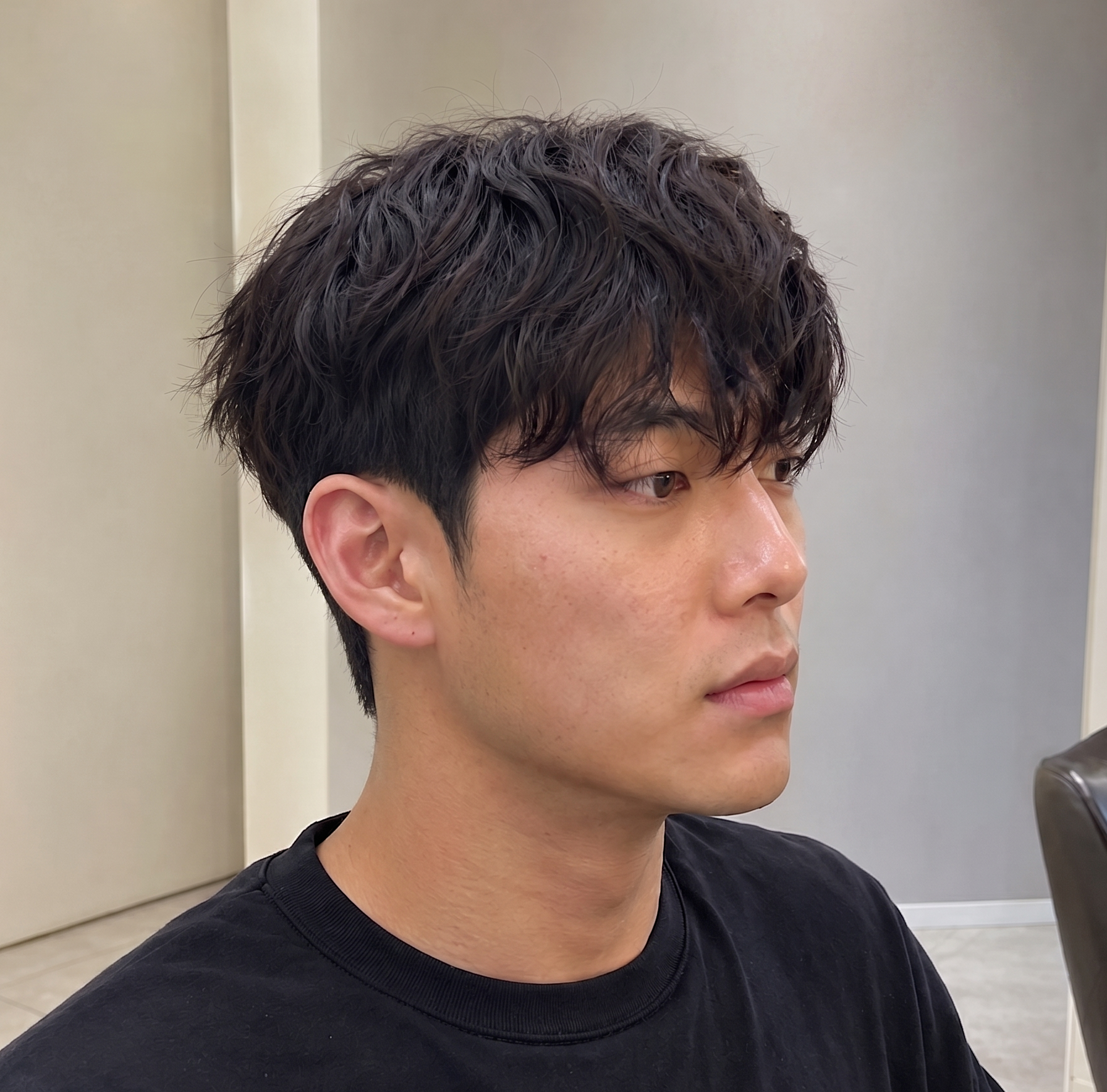Side-profile portrait of a person with short dark hair, wearing a black shirt, against a gray indoor wall at busan gwangalli haeundae