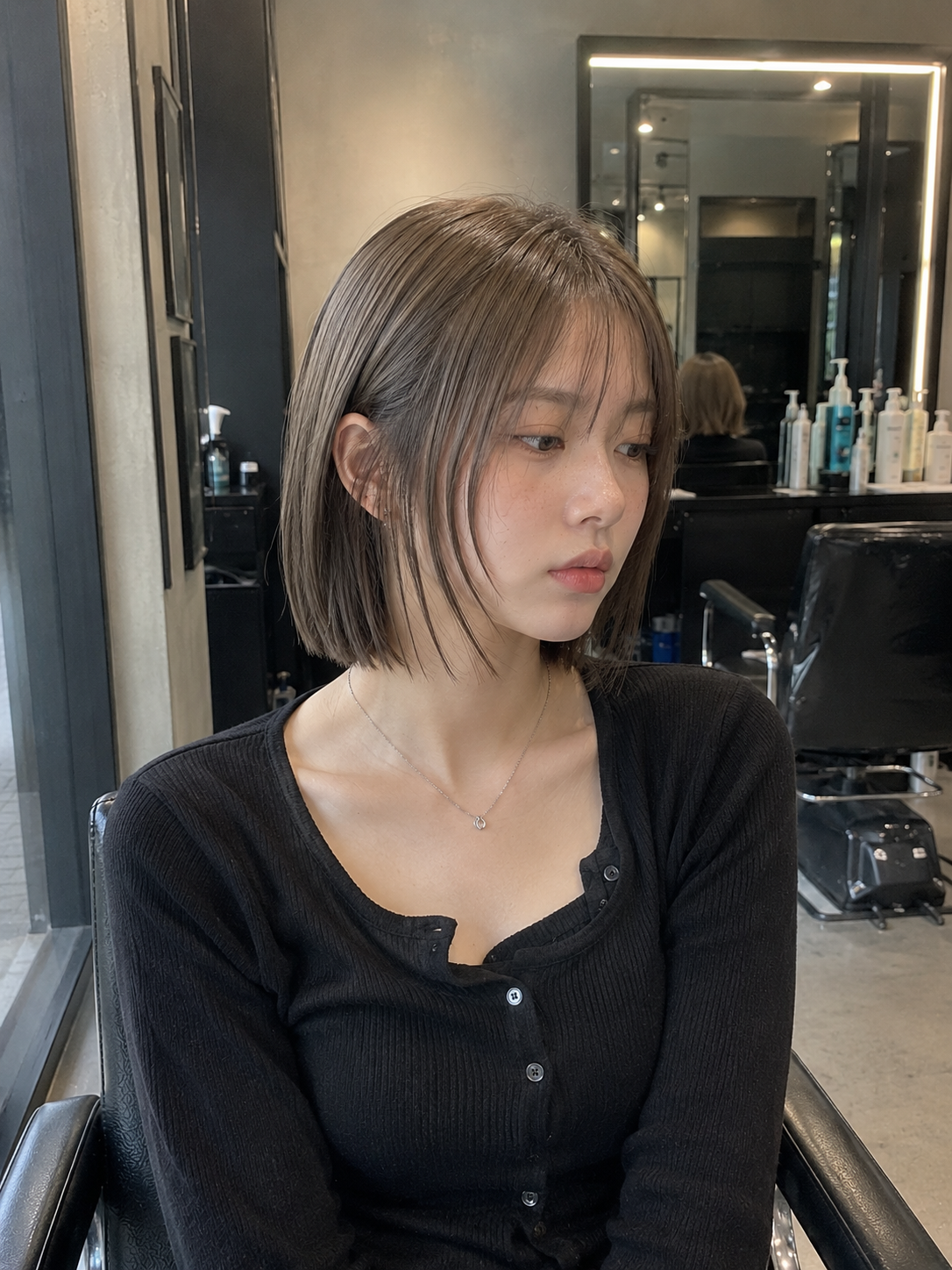 Young person with a short bob haircut seated in a salon, wearing a black top and looking to the side at busan gwangalli haeundae