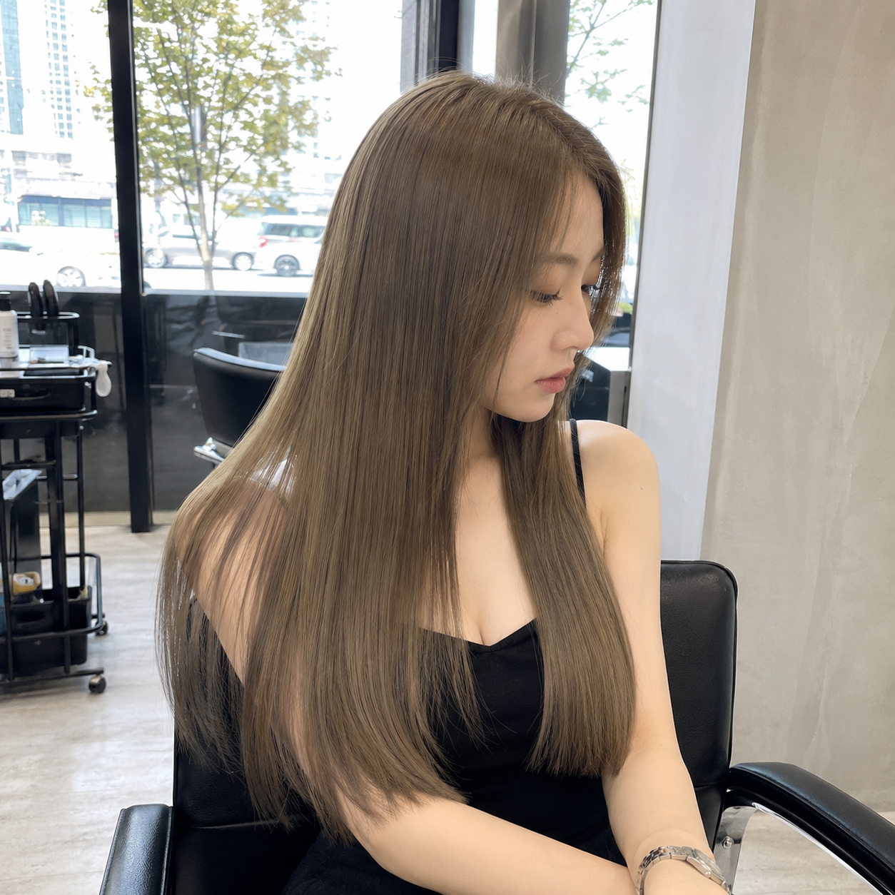 Woman with long brown hair seated indoors by a window, looking down in a black top at busan gwangalli haeundae