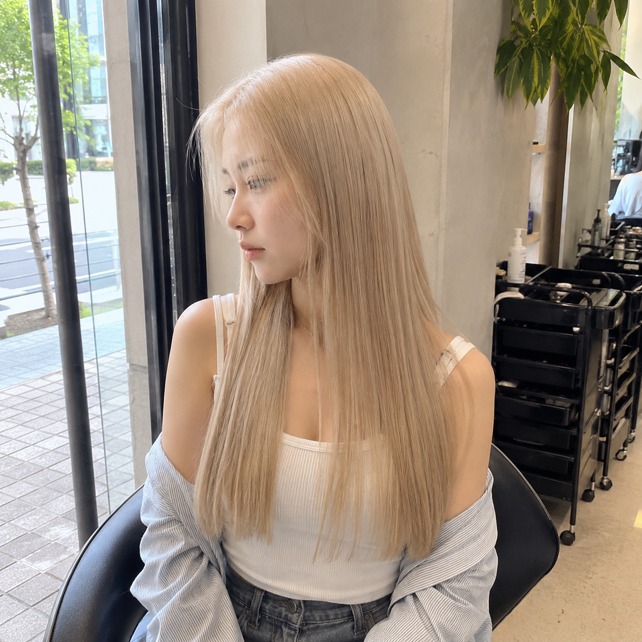 Woman with long blonde hair in a cafe, looking out a window in a white top and striped shirt at busan gwangalli haeundae
