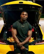Man standing in the open trunk of a yellow sports car, wearing a dark shirt, with bags in the trunk.