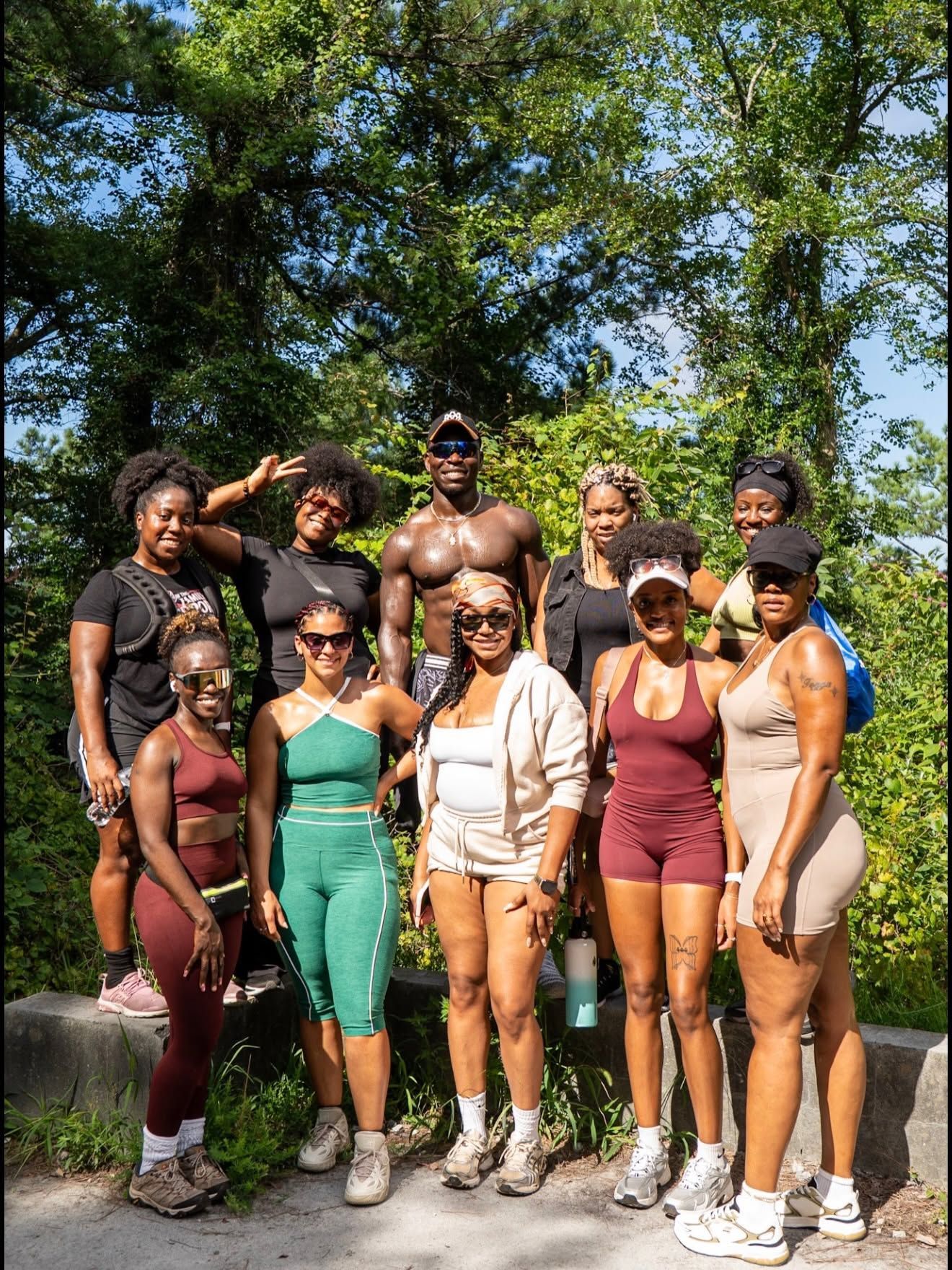 Group of eight hikers posing on a forest trail, wearing sporty outdoor outfits and backpacks.