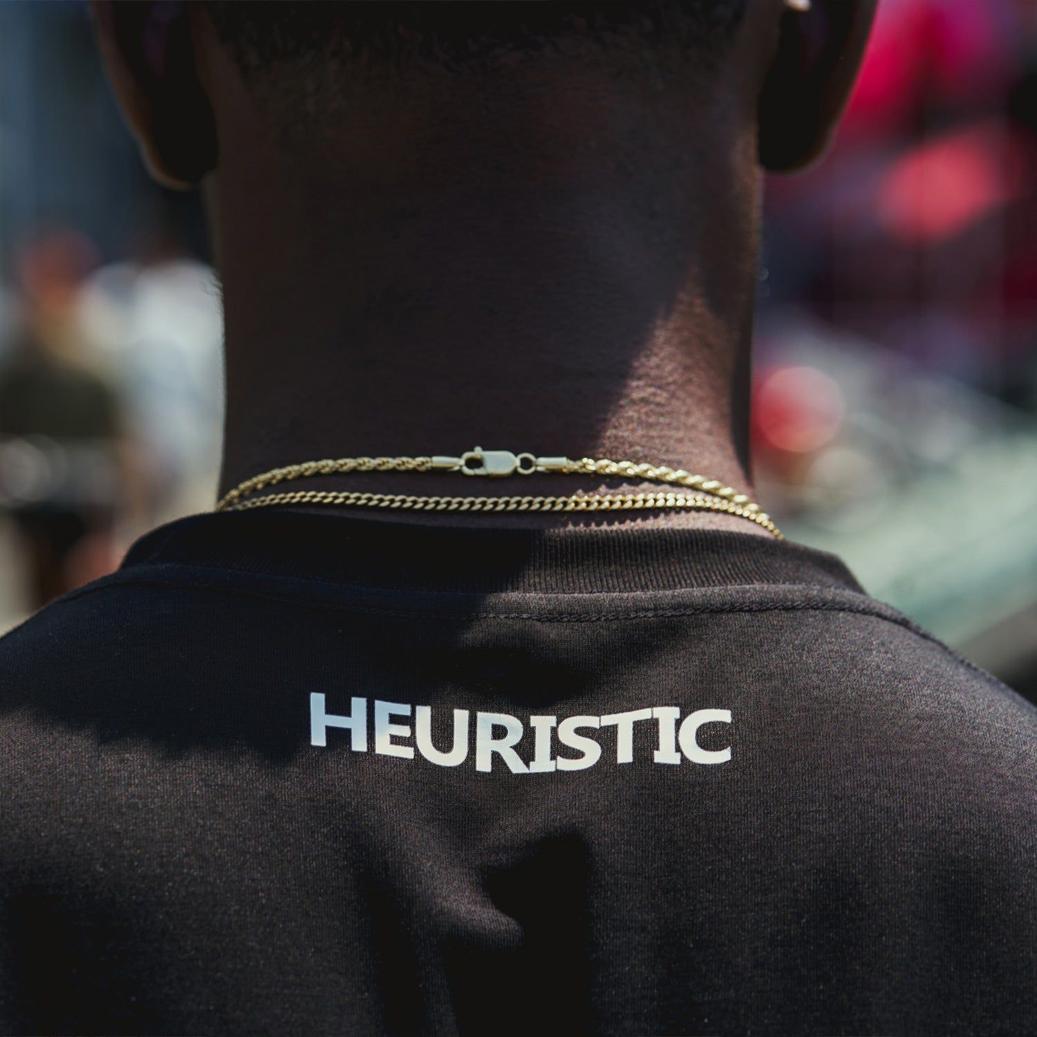 Back of a person wearing gold chains and a black shirt reading “HEURISTIC”