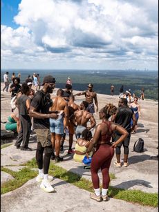 Crowd in swimwear gathered on a rocky overlook with the city skyline and water in the distance.