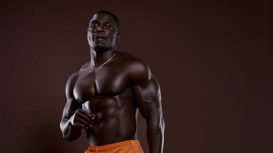 Studio portrait of a muscular man with a raised fist, wearing orange shorts against a dark background
