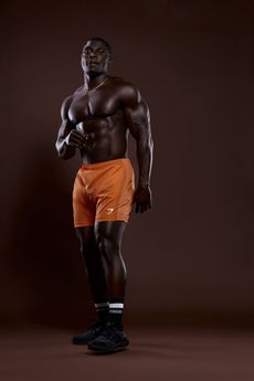 Athletic man in orange shorts and black shoes posing against a dark studio background