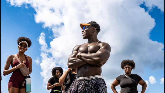 Four athletes standing outdoors under a blue sky, with one person centered and arms crossed.